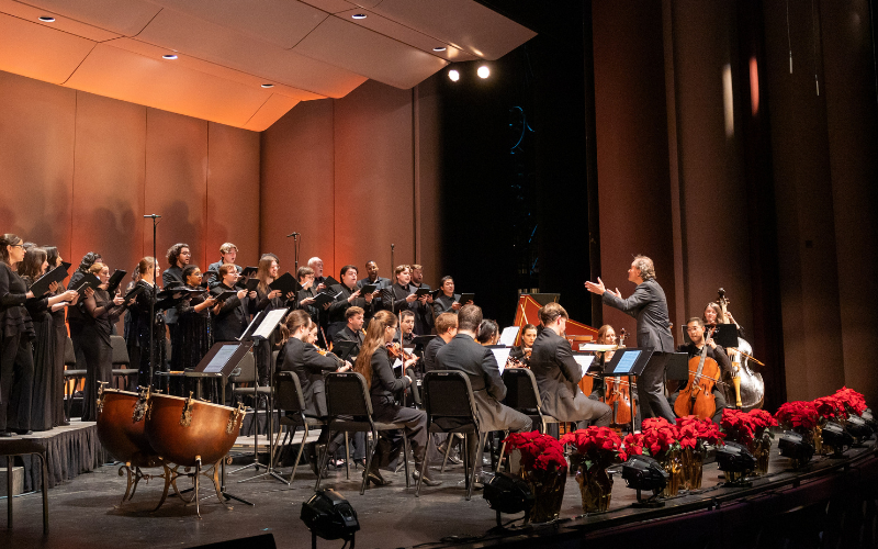 Choir and Orchestra on a stage lined with poinsettia plants