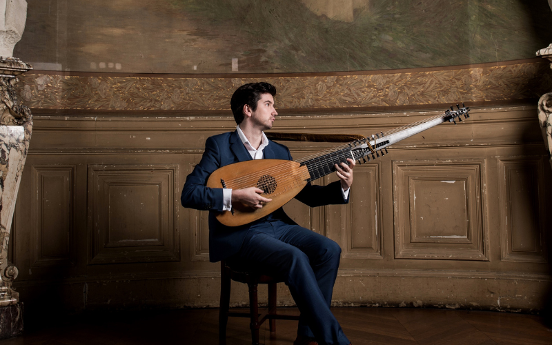 Man playing lute on a stool in a classical room