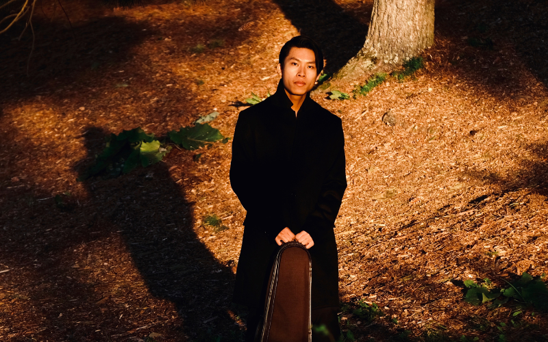 Man standing with violin amongst a sunlit forest