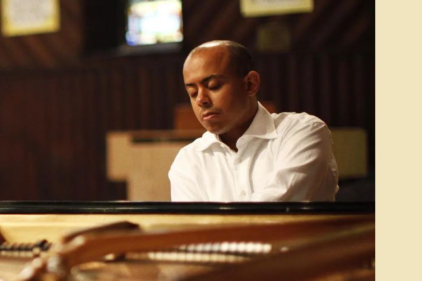 Black man in a white shirt eyes closed sitting at the piano
