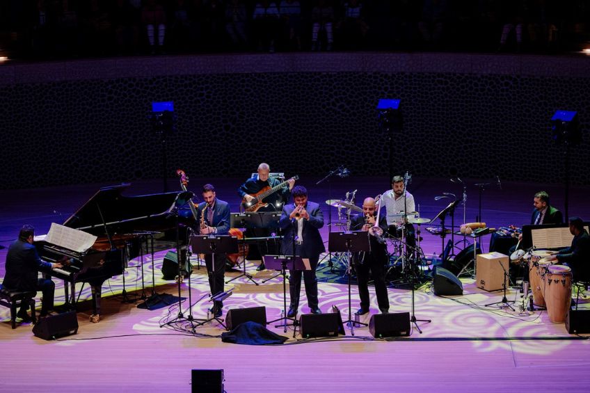 8 musicians on stage including drums, horns and piano