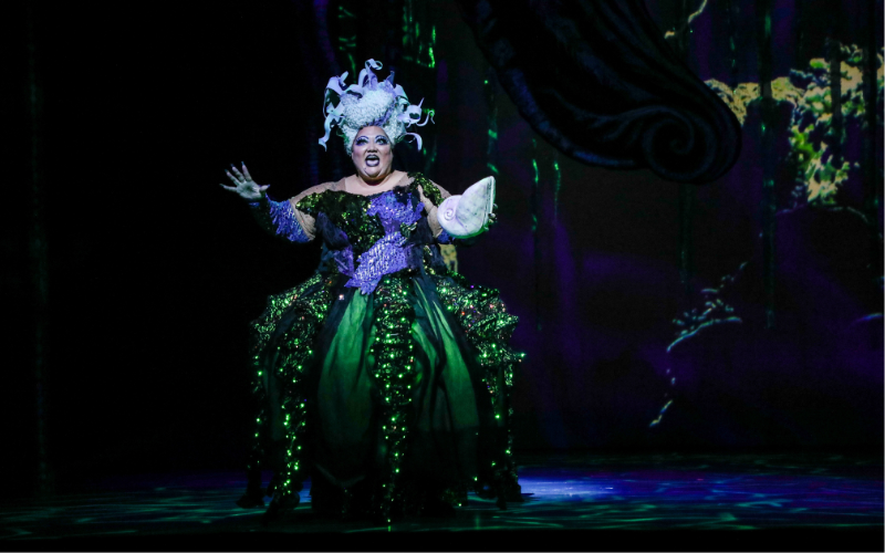Christina Wells as Ursula in Disney's The Little Mermaid, wearing a sparkling costume and holding a white seashell.